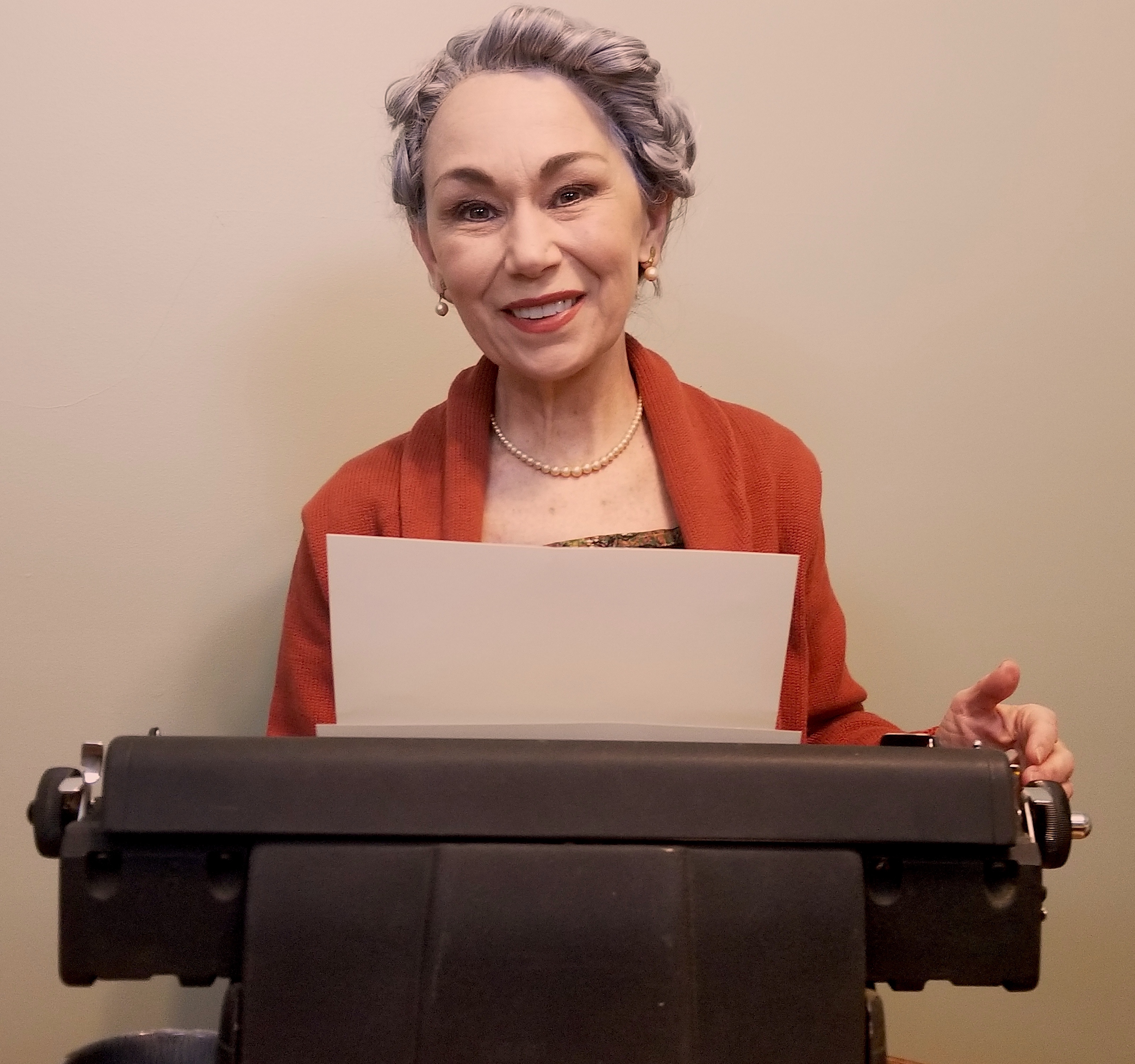 Debra Miller portraying Agatha Christie, seated in front of a typewriter