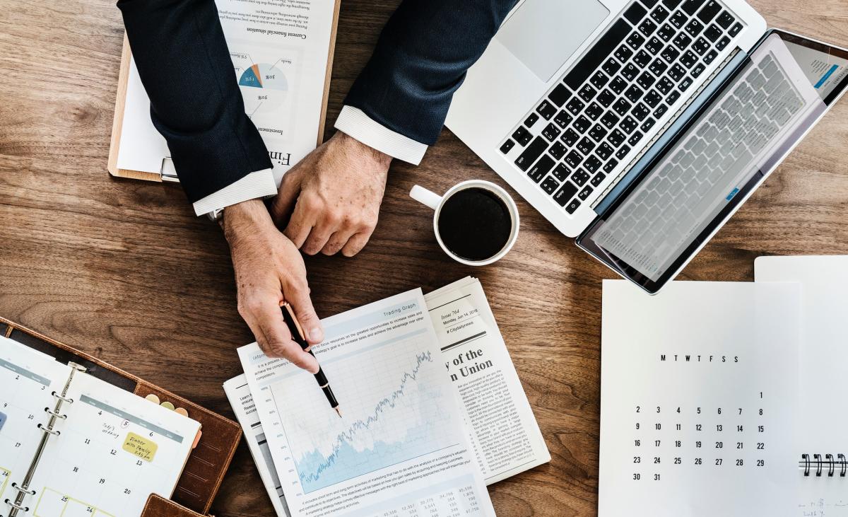 Financial reports spread out across table with man in business suit pointing at report with pen in hand