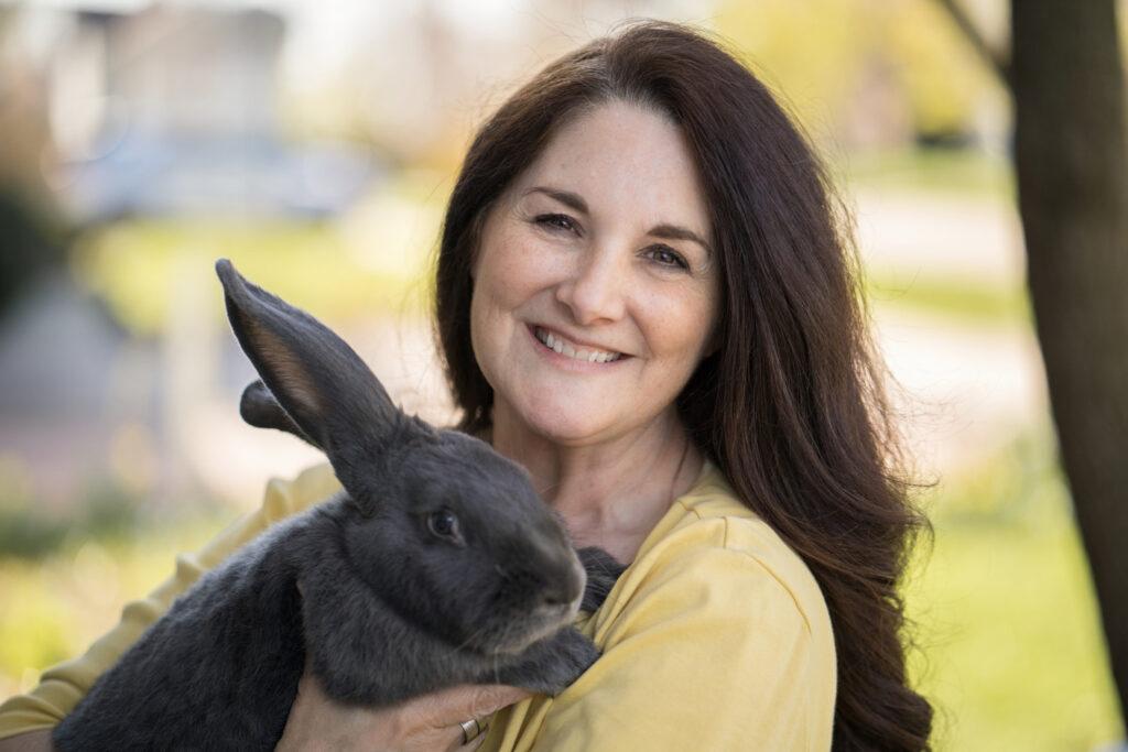 Photo of Kim White, a woman with long brown hair, holding a dark grey rabbit.